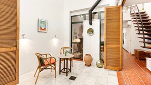 A room with a wooden door, a wicker chair, a small table, a vase, and a staircase. - Chalet 'Casa Limón' with Mountain View, Wi-Fi and Air Conditioning (Vélez-Málaga)