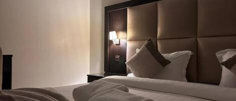 Et hotelværelse med en stor seng, en sengegavl og et natbord med en lampe.