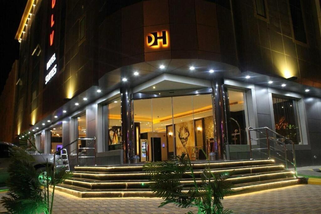 L'ingresso di un hotel con il logo DH ben visibile, una facciata in vetro e una scalinata illuminata che conduce all'entrata.
