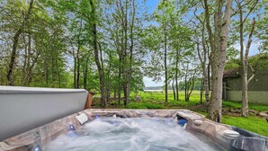 A hot tub surrounded by trees and a grassy area. - Modern Lake View, Firepit, Hot Tub, Lake Views! (Tobyhanna)