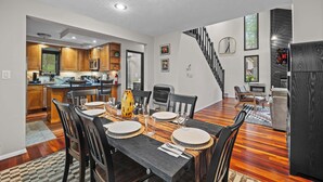A modern kitchen with wooden cabinets and a dining area with a black table and chairs. - Modern Lake View, Firepit, Hot Tub, Lake Views! (Tobyhanna)