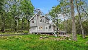 A two-story house with a porch, surrounded by trees and a grassy yard. - Modern Lake View, Firepit, Hot Tub, Lake Views! (Tobyhanna)