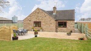 A stone house with a gravel patio, a wooden fence, and a grassy yard.