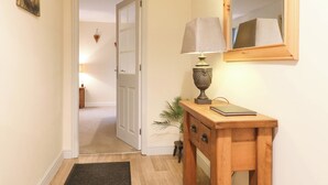 A hallway with a wooden console table, a lamp, a mirror, and a door leading to another room.