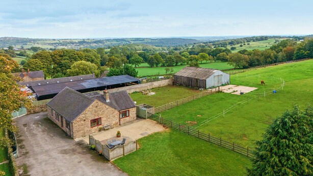 A rural farmstead with stone buildings, a fenced pasture, and rolling hills in the background.