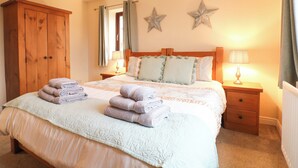 A neatly made bed with folded towels, a wooden wardrobe, two bedside lamps, and star-shaped wall decorations.