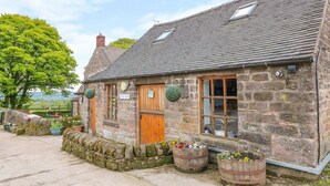 A stone cottage with a wooden door, two windows, and a stone wall. - The Barn (Matlock)