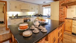 A kitchen with a central island, wooden cabinets, and a brick wall. - The Barn (Matlock)