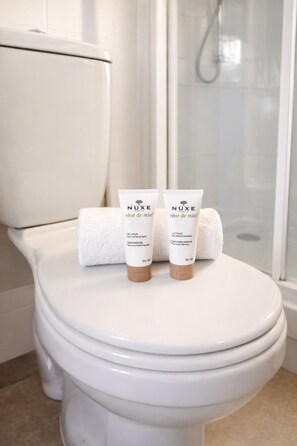 A white toilet with two Nuxe skincare tubes and a white towel on the lid. - 841 Polytech (Paris)