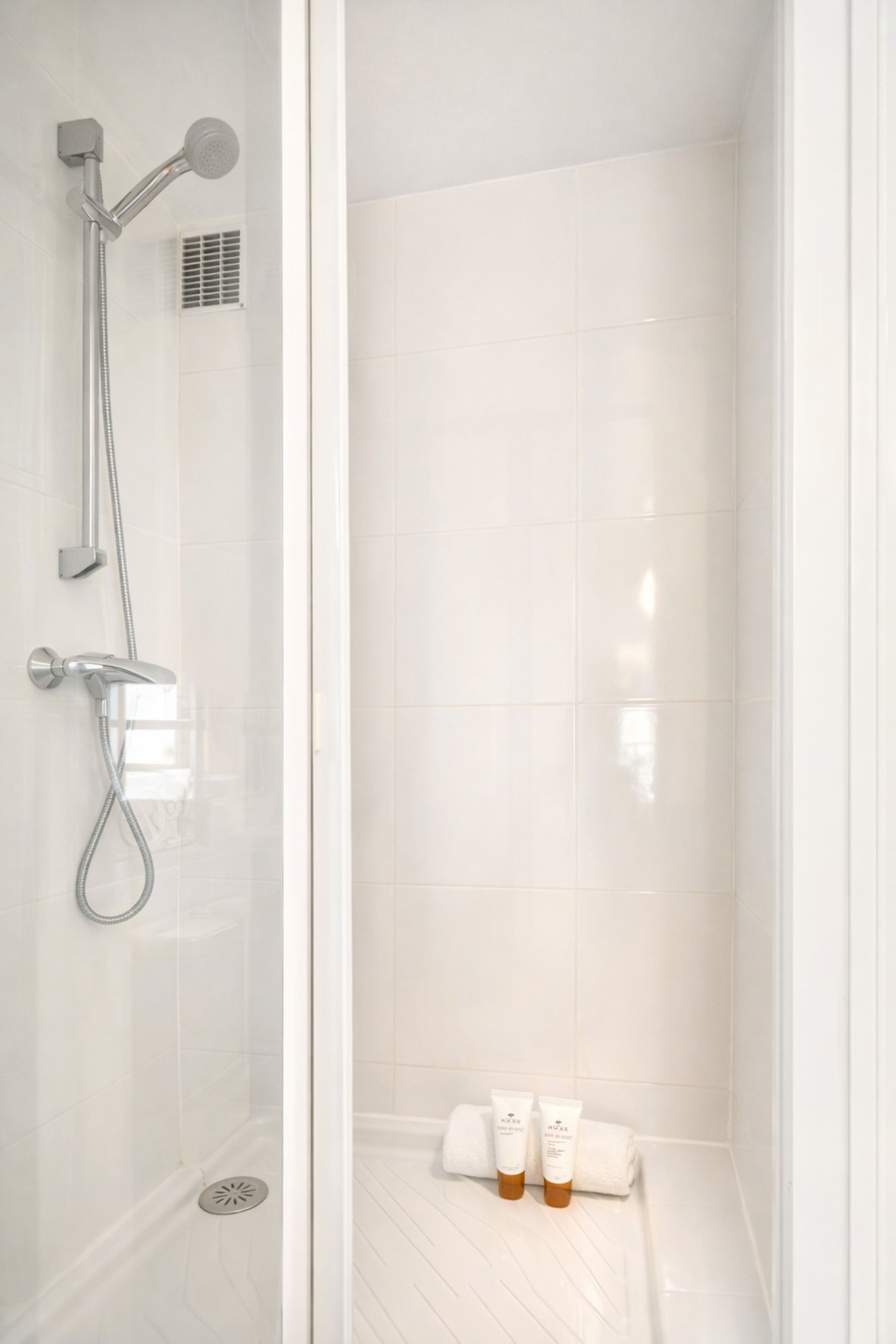 A modern shower with a glass enclosure, a handheld showerhead, a wall-mounted showerhead, and a vent.