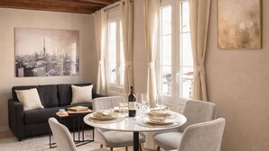A dining area with a round table, chairs, a sofa, and a cityscape painting on the wall. - 841 Polytech (Paris)