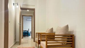Un pasillo con un banco de madera, un tapete rojo estampado y una puerta que da a una habitación con una cama y un escritorio.
