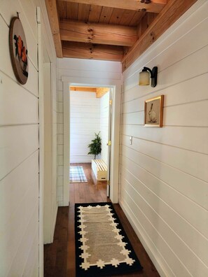 A hallway with wooden beams, white walls, a black and white rug, a bench, and a framed picture.
