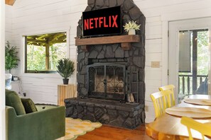 Una sala de estar acogedora con chimenea de piedra, un cartel de Netflix y vistas al exterior.