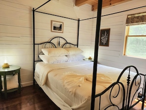 A four-poster bed with white bedding, two bedside tables with lamps, and a window with a view of trees. - Romantic Log Cabin • Hot Tub • Fireplace • View (Logan)