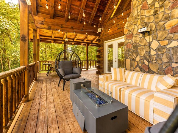 Una terraza de madera con una pared de piedra, un sofá, una silla y una mesa con cubierta de vidrio.