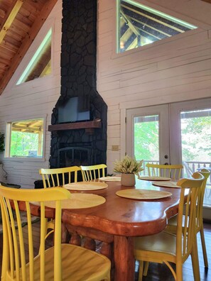 Un espace repas agrémenté d’une cheminée en pierre, d’un plafond en bois et de grandes fenêtres.