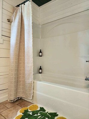 Une salle de bain avec une baignoire, un rideau de douche et deux bouteilles posées sur une étagère.