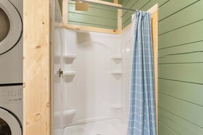 Lavandería con lavadora, secadora y cabina de ducha con cortina azul.