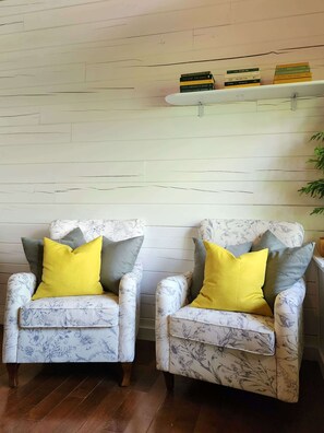 Two armchairs with floral upholstery and yellow and gray cushions, positioned against a white wooden wall with a shelf above holding books. - Romantic Log Cabin • Hot Tub • Fireplace • View (Logan)