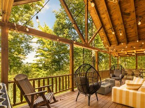 A wooden deck with outdoor seating, including chairs and a sofa, surrounded by trees. - Romantic Cabin: Hot Tub•Outdoor Movies•Fireplace (Logan)