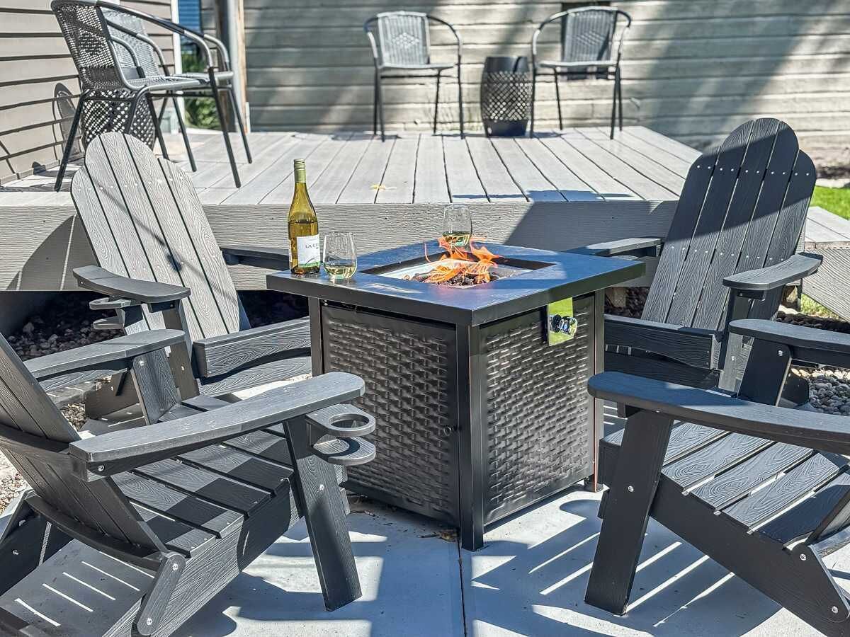 Une terrasse avec des fauteuils Adirondack, un foyer et une bouteille de vin.