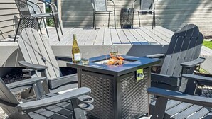 Een terras met Adirondack-stoelen, een vuurkorf en een fles wijn.