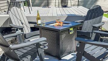 Eine Terrasse mit Adirondack-Stühlen, einem Feuerkorb und einer Weinflasche.