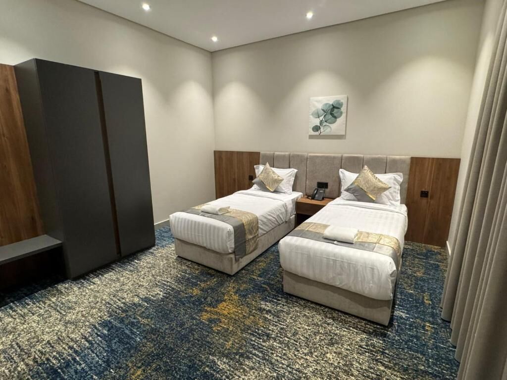 A hotel room with two beds, a wardrobe, a wall-mounted artwork, and a carpeted floor.