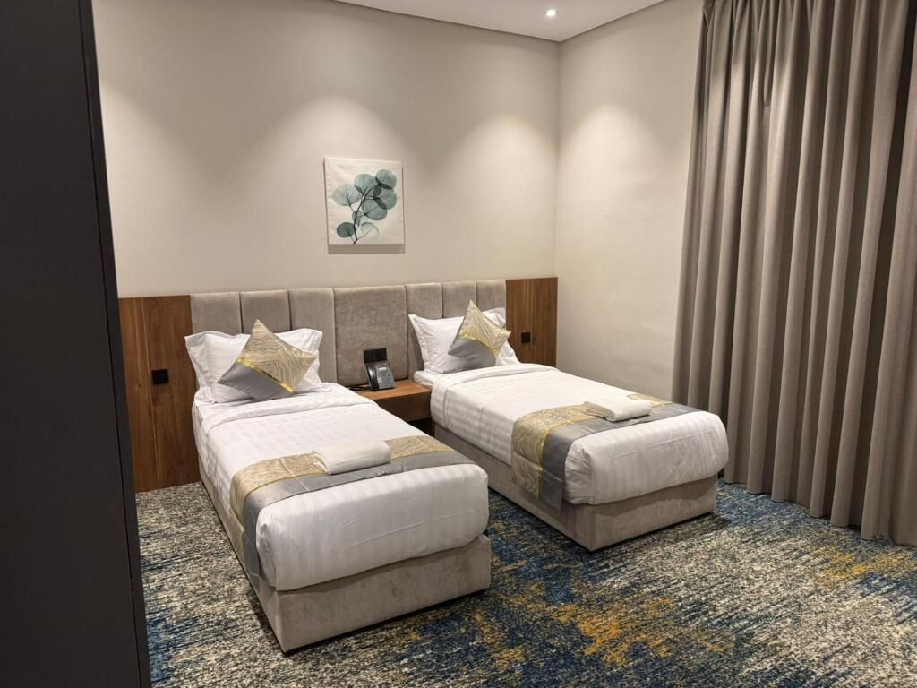 A hotel room with two beds, a headboard, a painting, a nightstand, and a window with curtains.