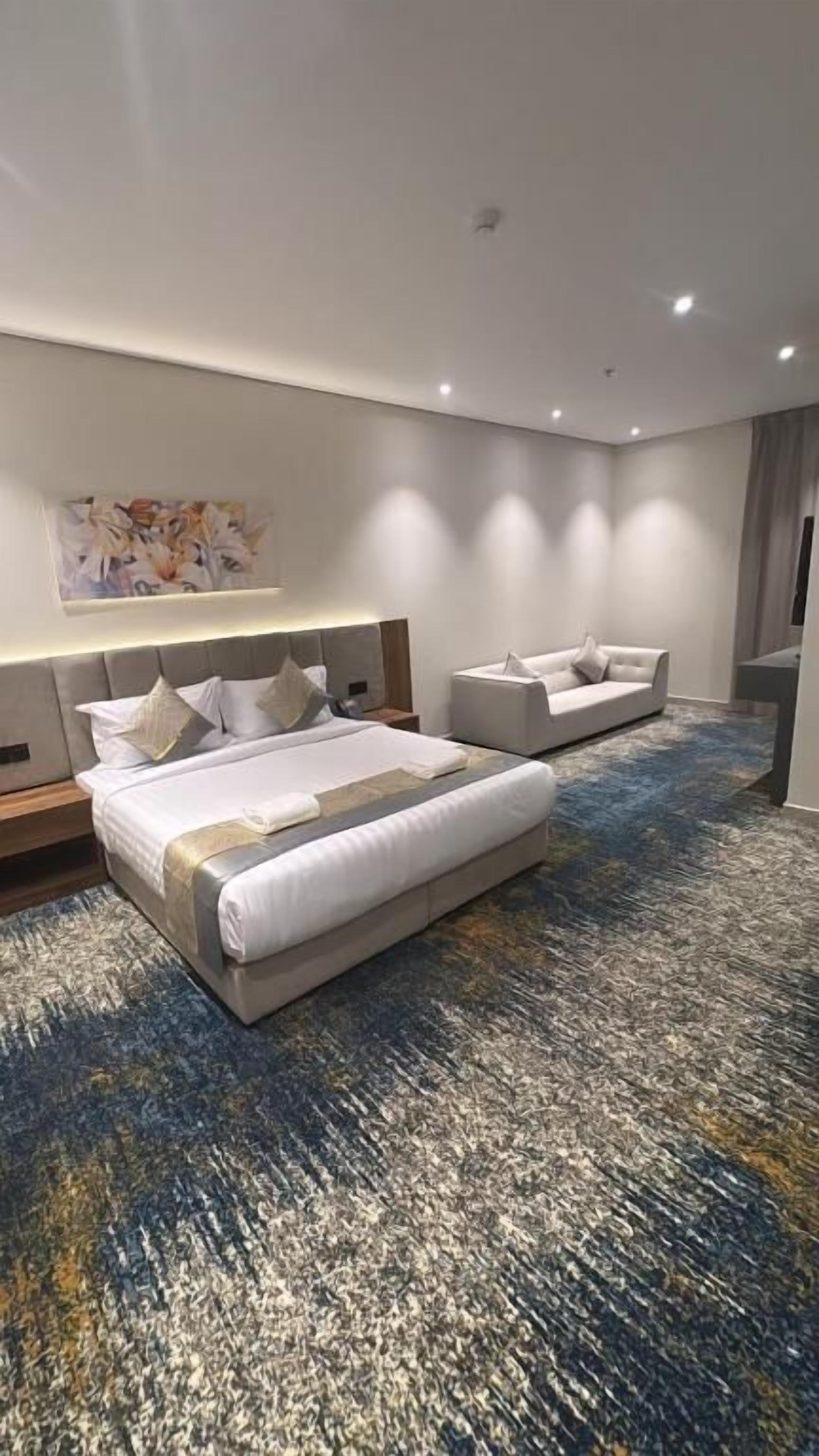 A modern hotel room with a large bed, a sofa, a desk, and a TV.