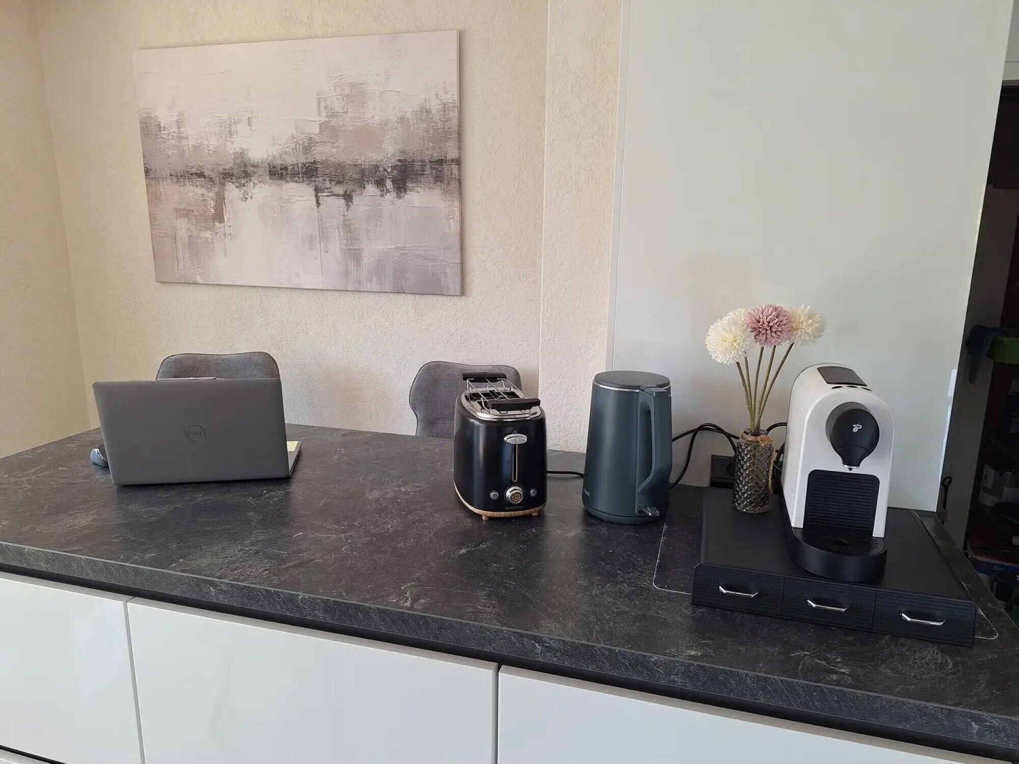 A kitchen counter with a laptop, toaster, kettle, and a speaker.