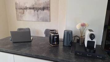 A kitchen counter with a laptop, toaster, kettle, and a speaker.