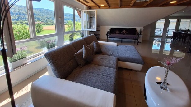 A modern living room with a sectional sofa, a white coffee table, and large windows offering a view of the outdoors. - Apartment 'Pure Vista' with Black Forest View, Private Terrace and Wi-Fi (Laufenburg)