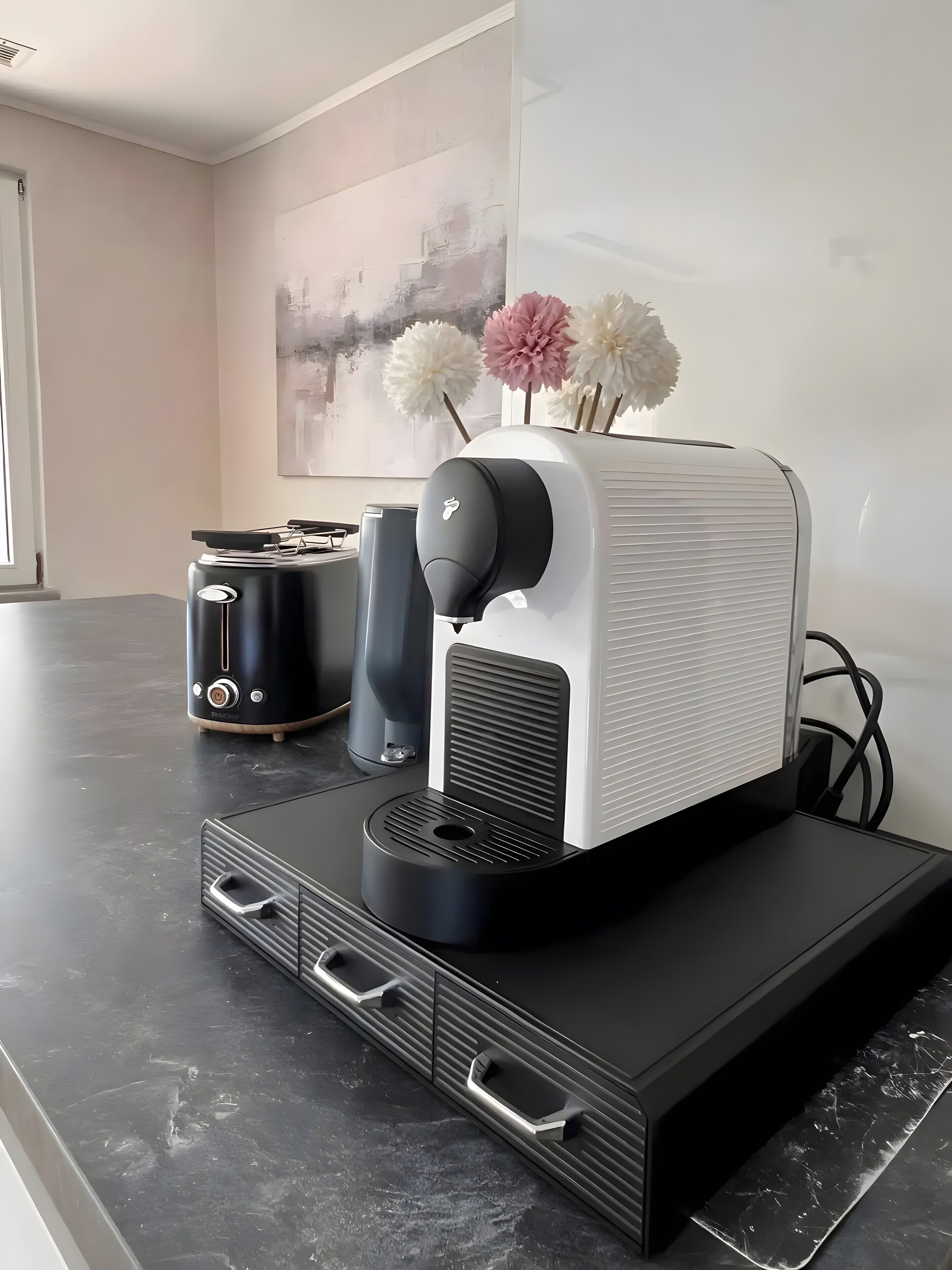 Et køkken med kaffemaskine, brødrister og elkedel på en sort bordplade.