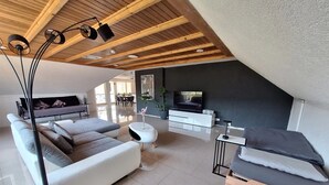 A modern living room with a high ceiling, a sofa set, a TV, and a dining area visible through a glass wall. - Apartment 'Pure Vista' with Black Forest View, Private Terrace and Wi-Fi (Laufenburg)