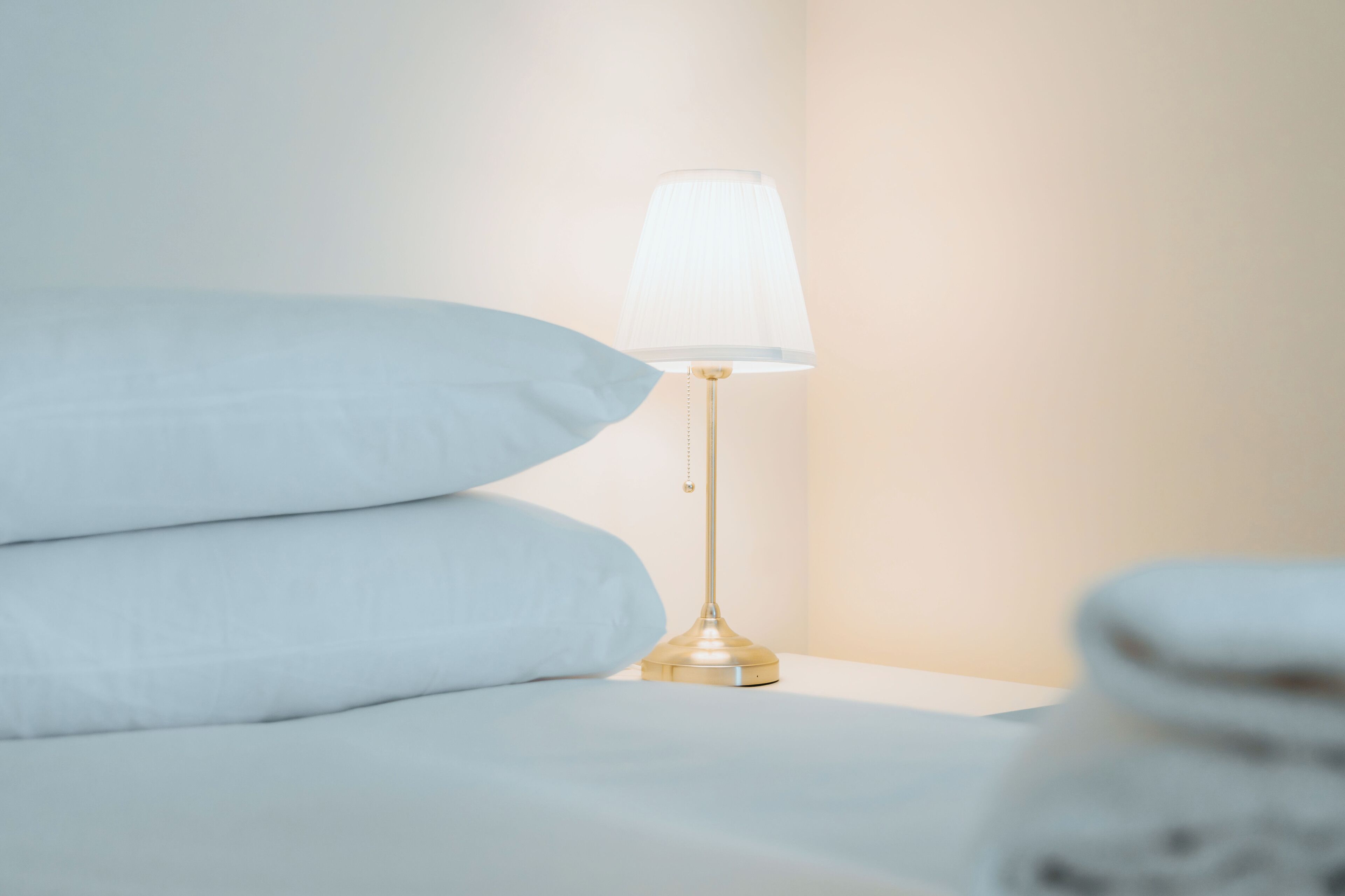 Un lit avec une table de chevet dorée et une lampe blanche.