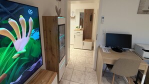 Habitación con una televisión de pantalla plana grande, un mueble de madera, un escritorio con computadora y una silla.