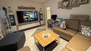 Una sala de estar con un televisor de pantalla plana grande, una mesa de centro de madera, un sofá marrón y un escritorio con una computadora.