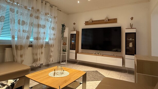 Una sala de estar moderna con un televisor de pantalla plana grande, una mesa de centro de madera y un sofá.