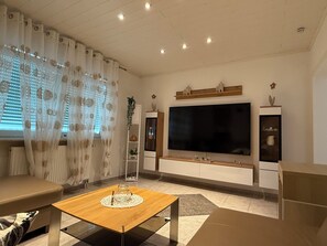 A modern living room with a large flat-screen TV, wooden coffee table, and a sofa.