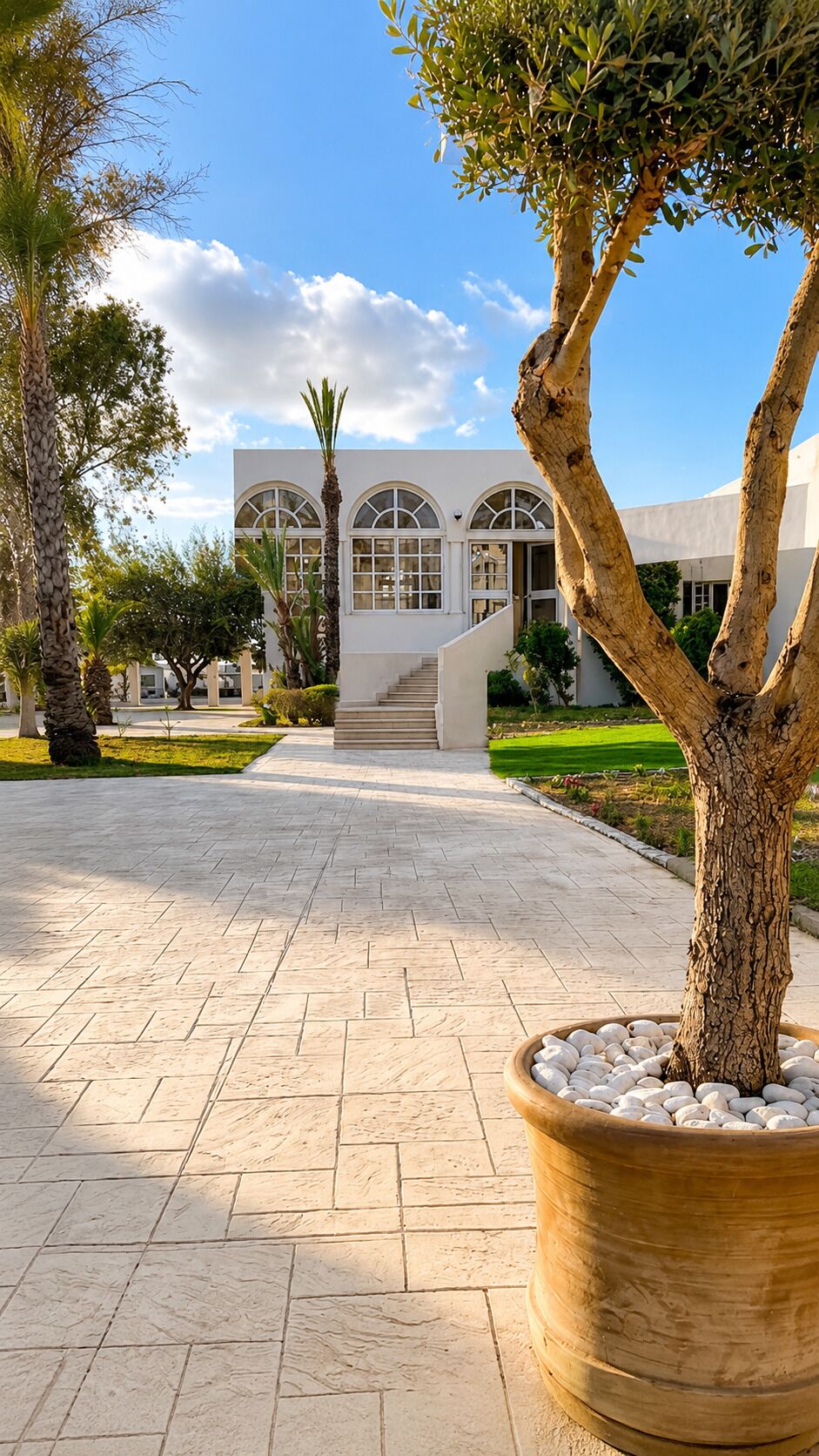 A paved walkway leading to a building with arched windows and a staircase.
