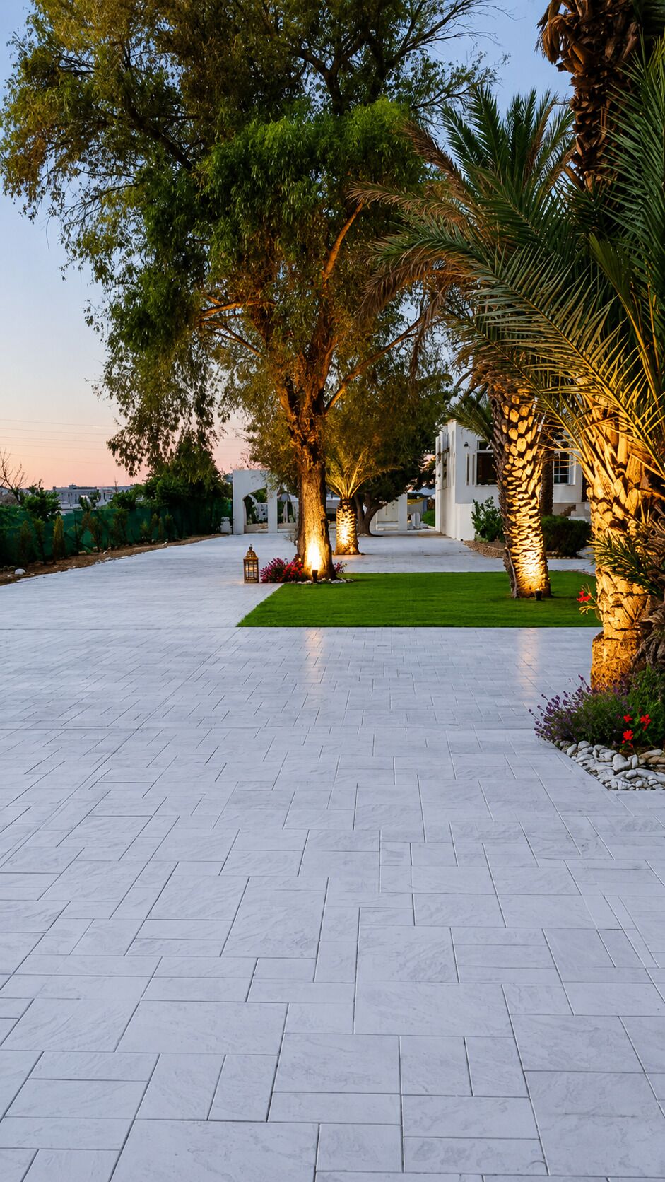 Un chemin pavé mène à un bâtiment blanc doté d’une entrée couverte, le tout étant entouré d’arbres et de plantes tropicales.