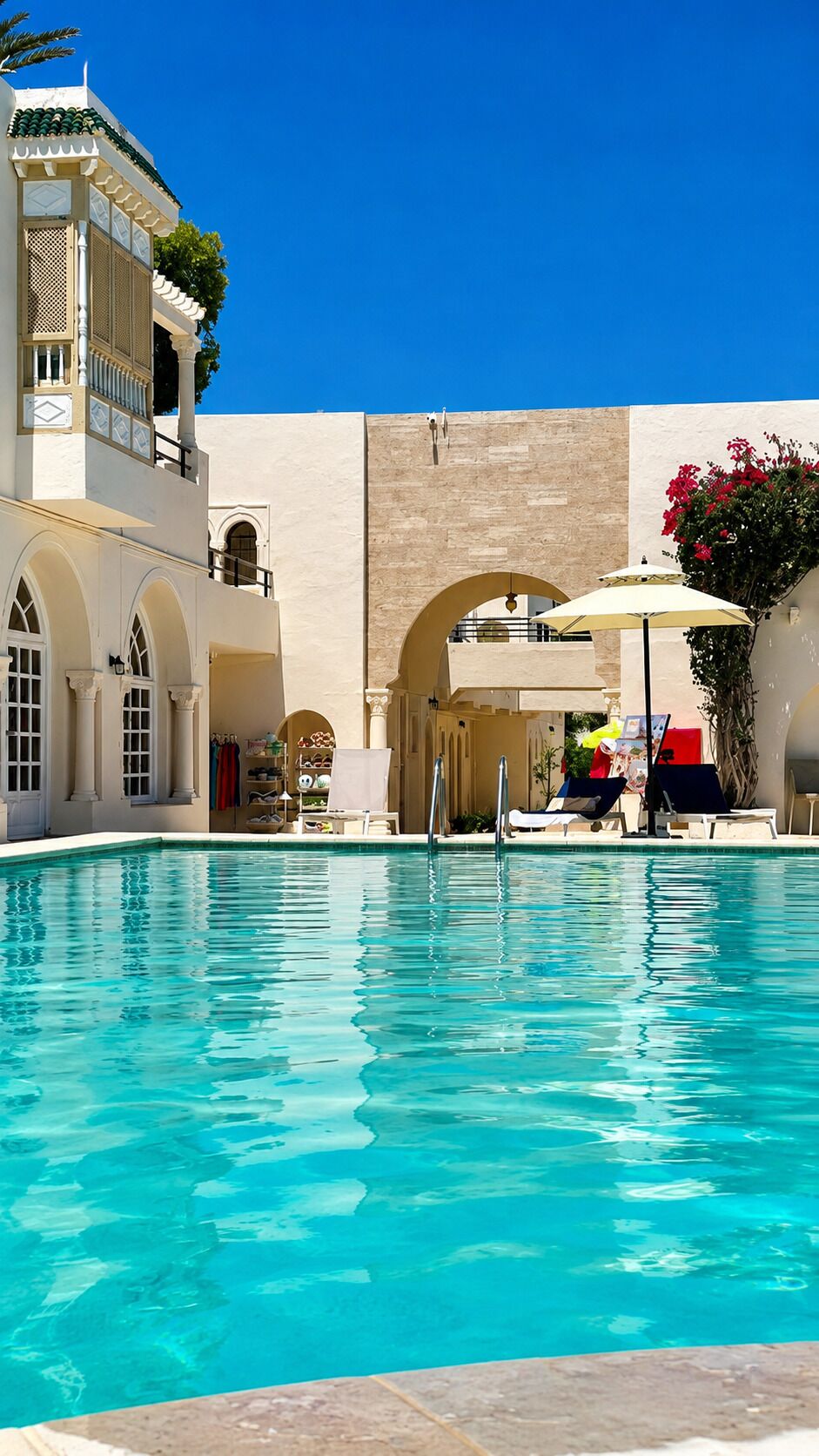 A swimming pool with clear blue water, surrounded by a building with arches and a balcony.