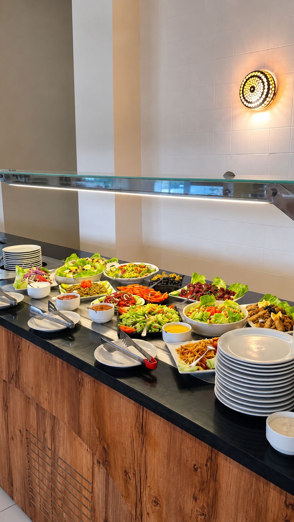Buffet amb diversos plats, incloses amanides i verdures, i una barana de vidre al fons.