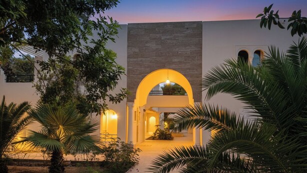 Un edificio con un arco central, un sendero que lo conduce y abundante vegetación circundante.