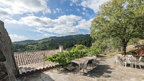 A terrace with a table and chairs, a view of a vineyard, and a stone wall. - Holiday Home 'La Casita' with Mountain View, Private Terrace (Beauvène)