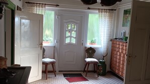 Una habitación con suelo de baldosas, una puerta blanca con panel de vidrio, una silla de madera, un tapete rojo y una araña.
