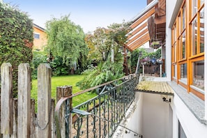 Un balcon doté d’une balustrade en fer forgé, d’une clôture en bois et d’un jardin où poussent diverses plantes et un arbre.
