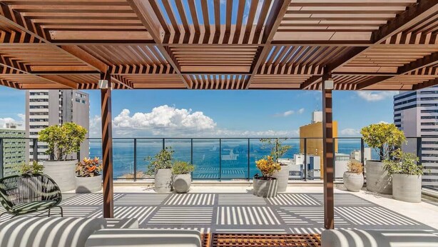 Una terraza en la azotea con una pérgola de madera, plantas en macetas y vista al mar.